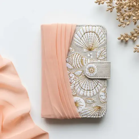 A peach chiffon-over-canvas passport cover with seashell embroidery in white and gold.