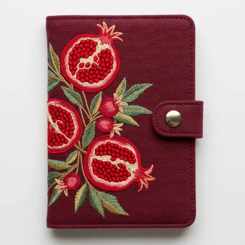 A burgundy organic cotton passport cover with pomegranate embroidery in red and gold.
