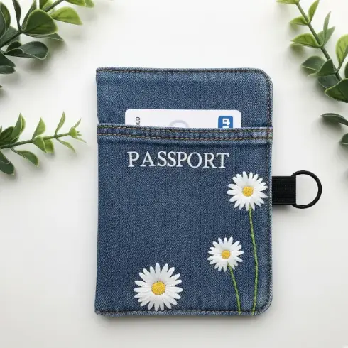 A recycled denim passport cover with hand-stitched white daisies.
