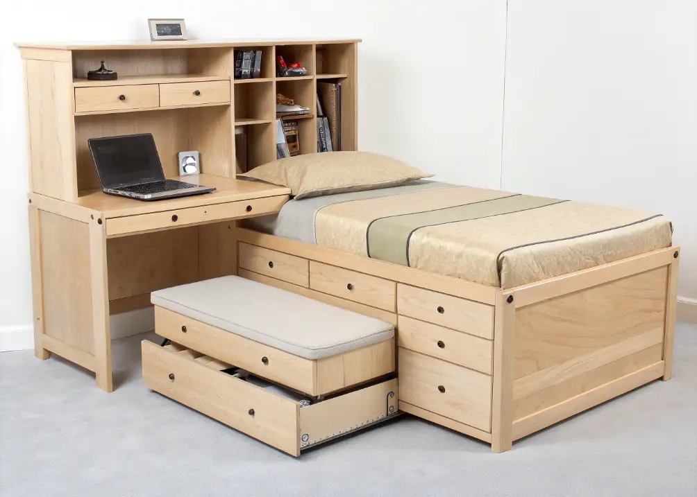  A platform bed with built-in drawers, a sleek fold-down desk in the corner, and a storage ottoman at the foot of the bed, all in light wood tones.